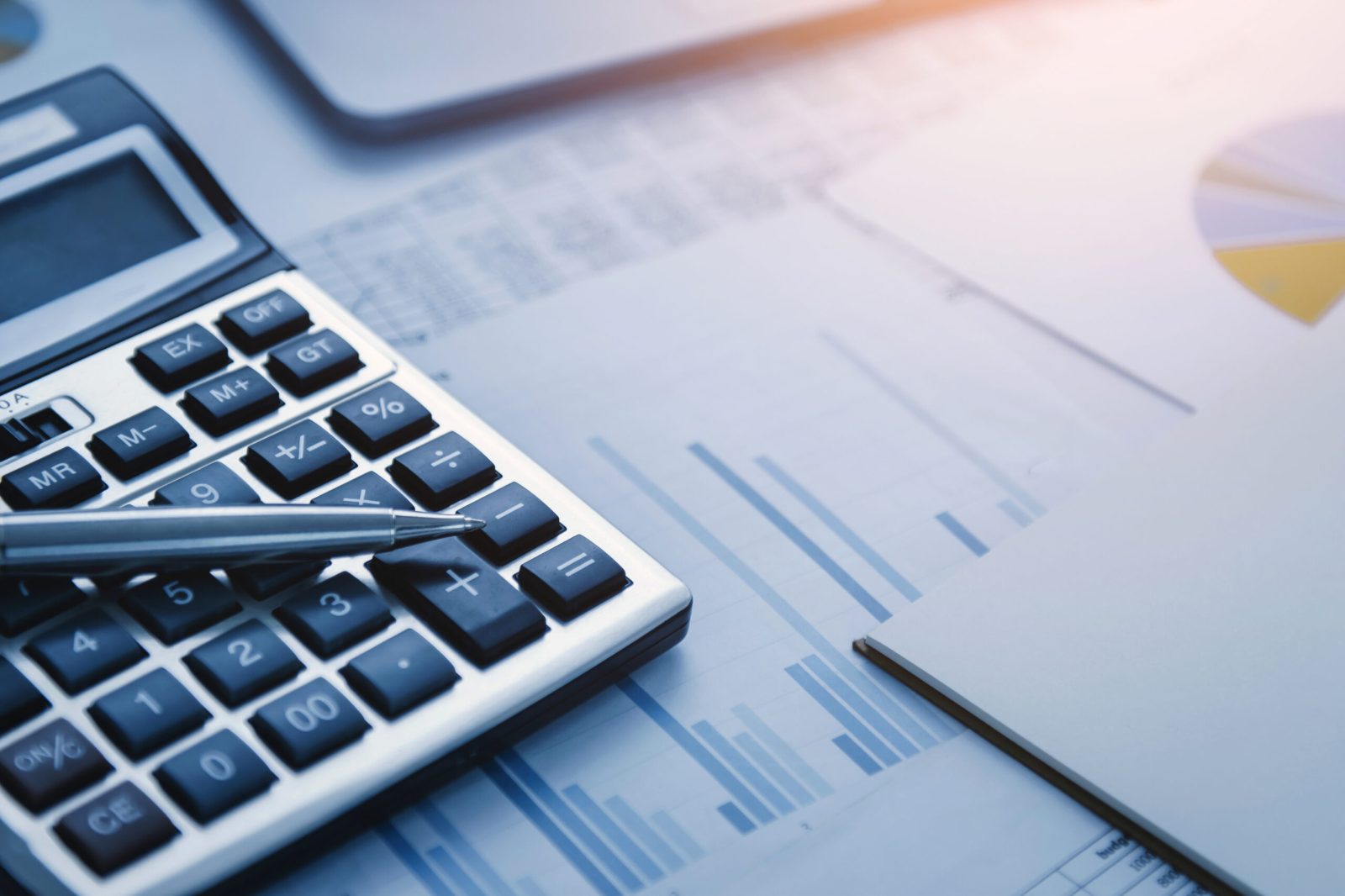 Calculator and pen resting on printed financial charts in a cool blue light