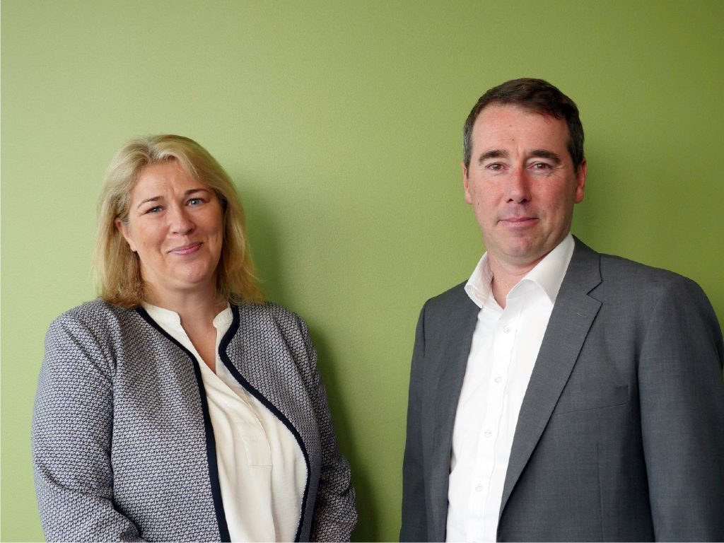 Joanne Smith and Adrian Fisk standing side by side against a green wall