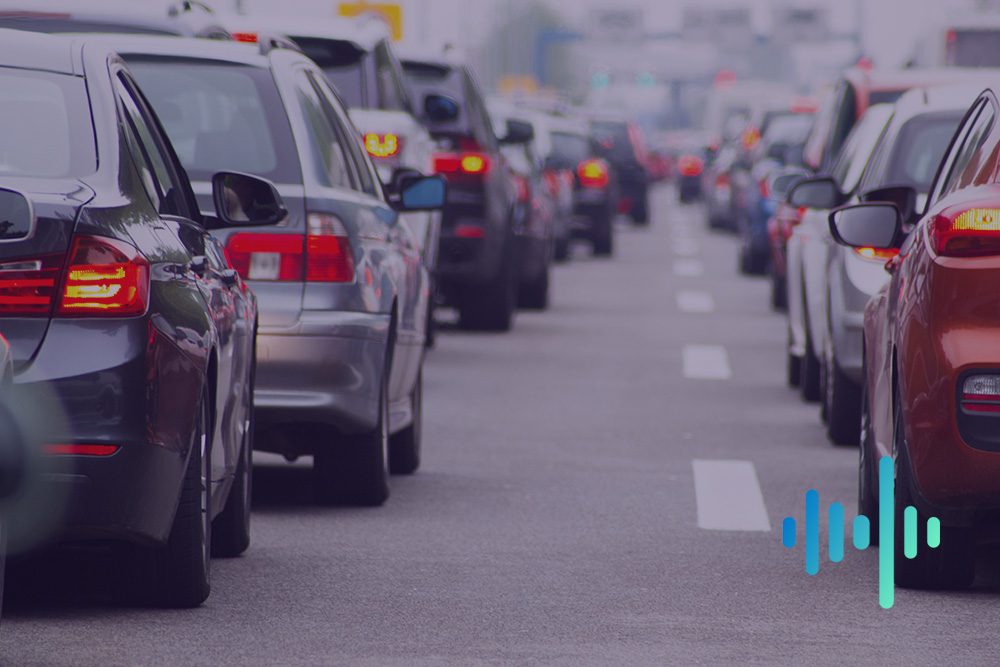 Queues of cars in slow-moving city traffic with red brake lights, with a blue and teal waveform