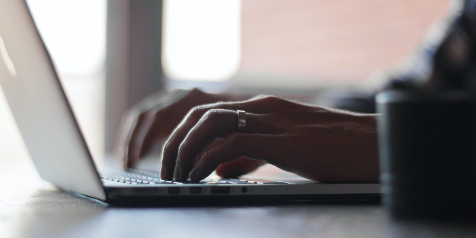 Close-up of hands typing on a silver laptop keyboard in soft, muted light