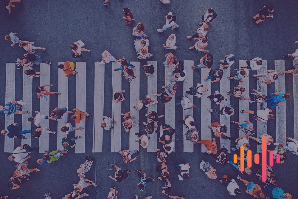 Aerial view of crowds of people crossing a wide zebra crossing, with an orange and pink waveform
