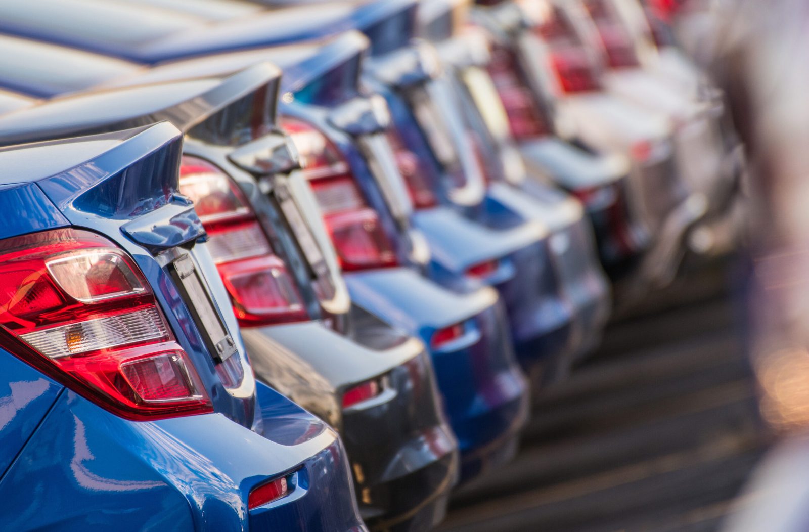 Rear view of a line of new blue and red cars parked at a dealership
