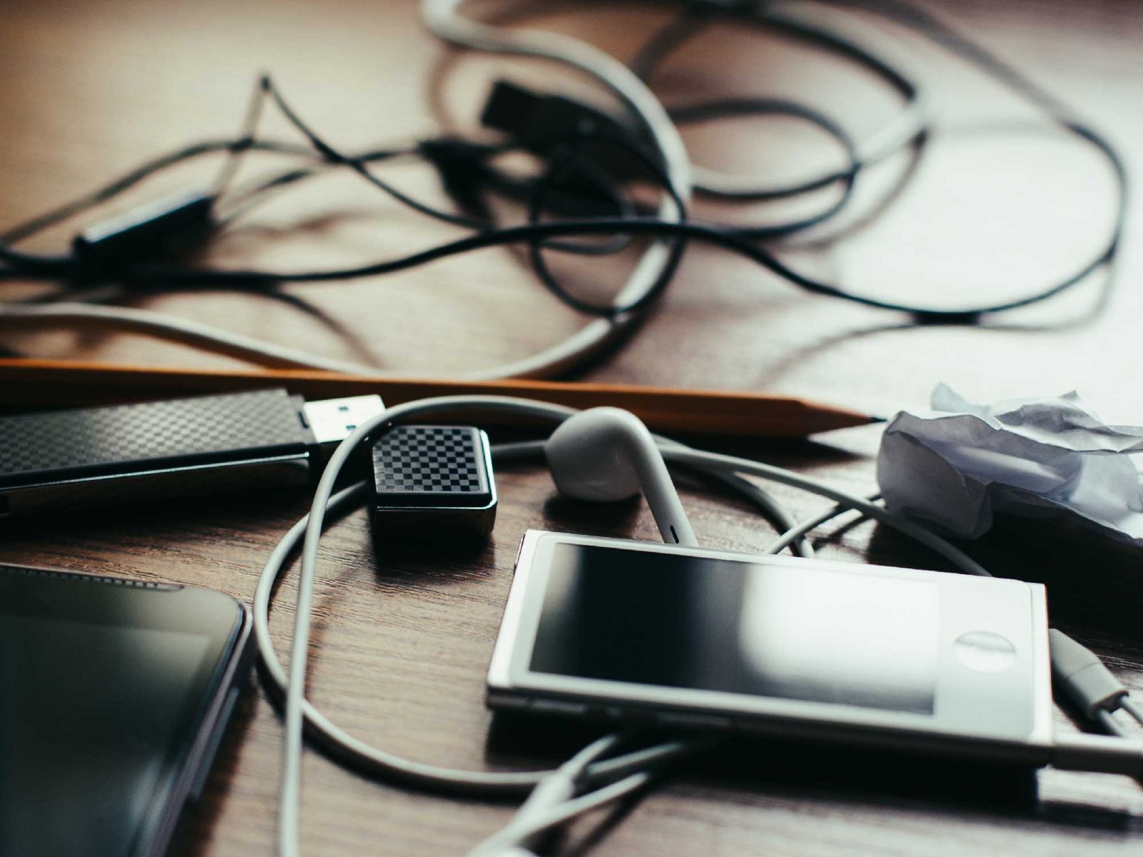 Tangle of charging cables, earphones and devices on a wooden desk