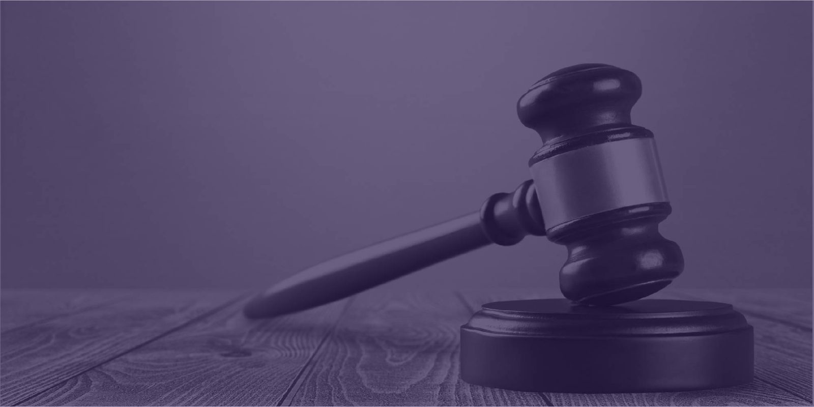 Judge's gavel resting on its block on a wooden table, under a purple tint
