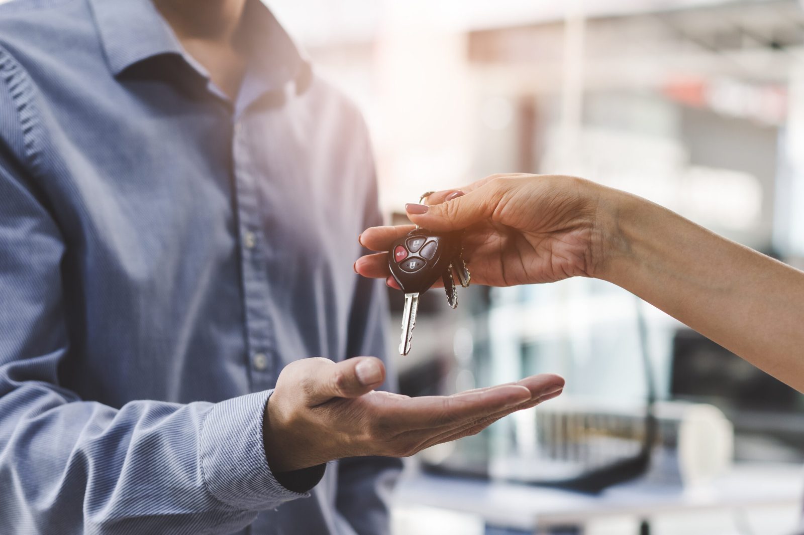 Car key being handed over into a customer's open palm in a car dealership
