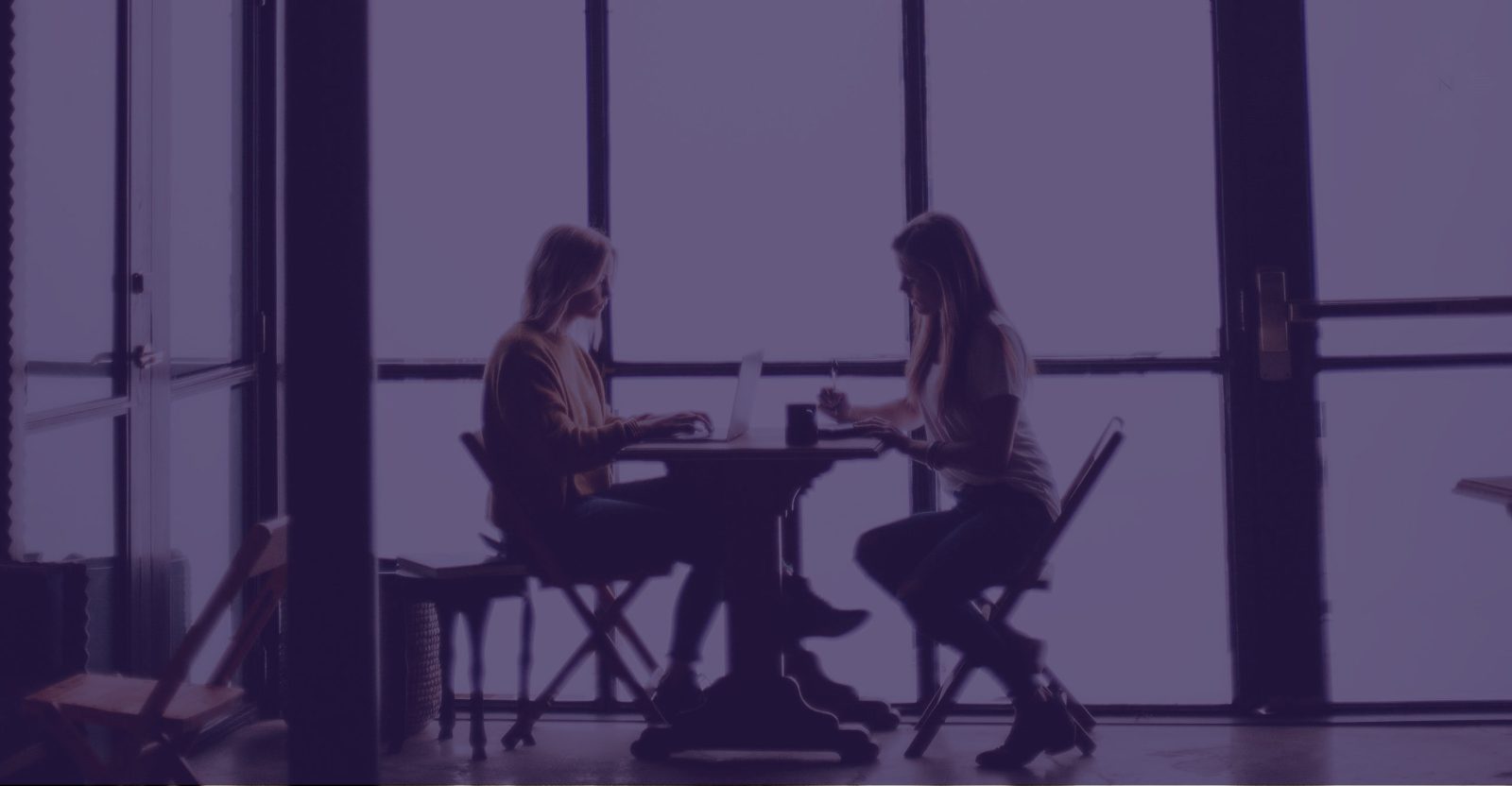 Silhouettes of two women talking at a table in front of tall windows, with a purple tint