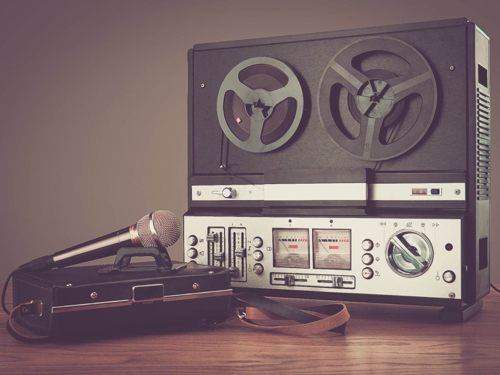Vintage reel-to-reel tape recorder with a microphone resting on a wooden table