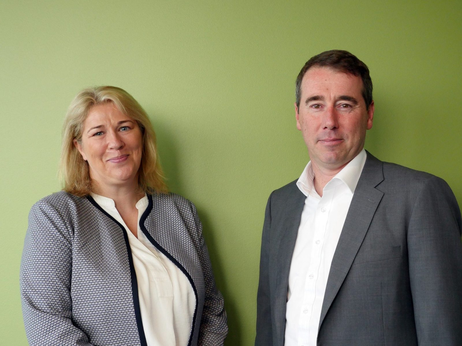 Joanne Smith and Adrian Fisk standing side by side against a green wall