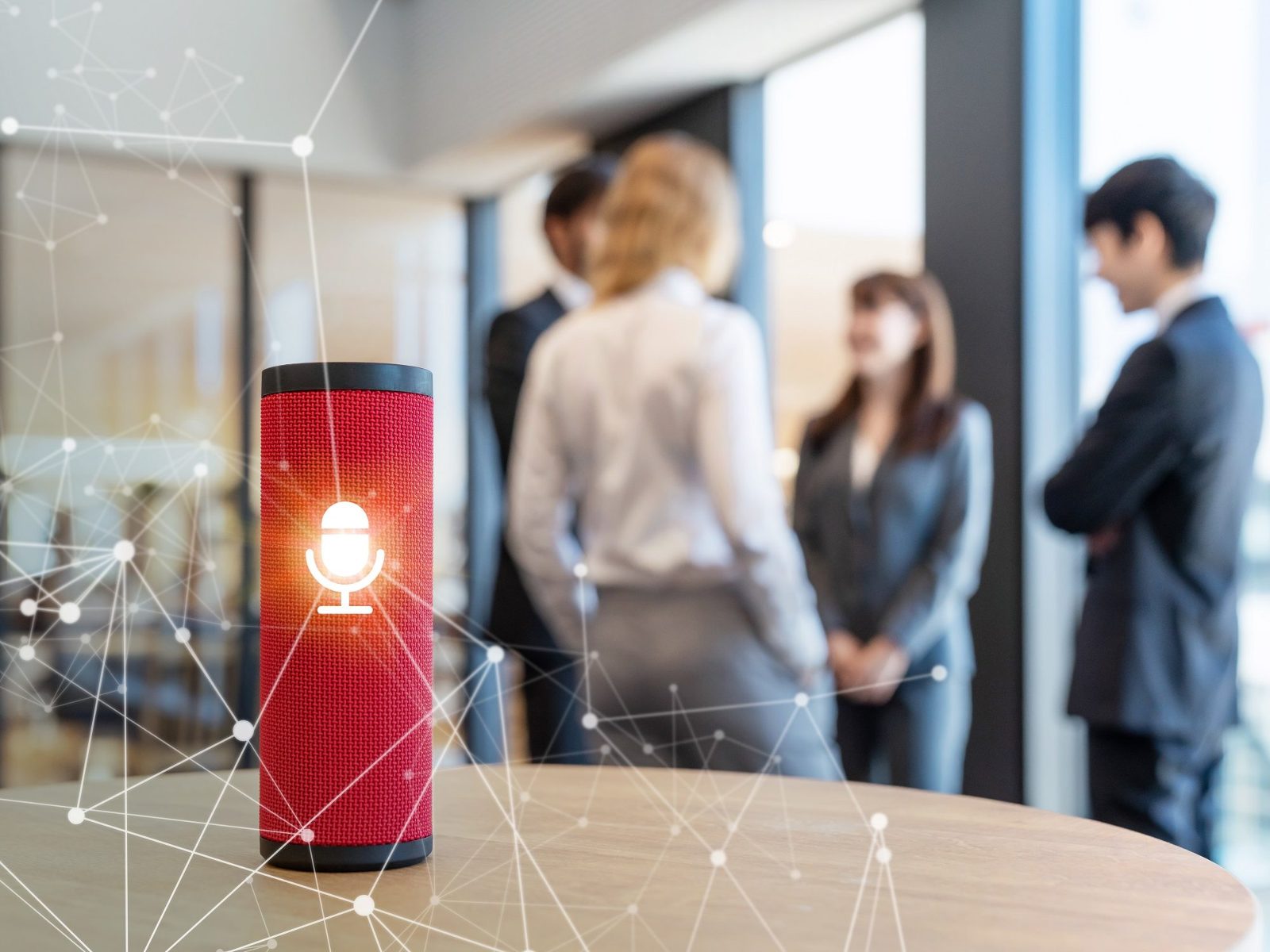 Red smart speaker glowing with a microphone icon on a table while business people talk in the background