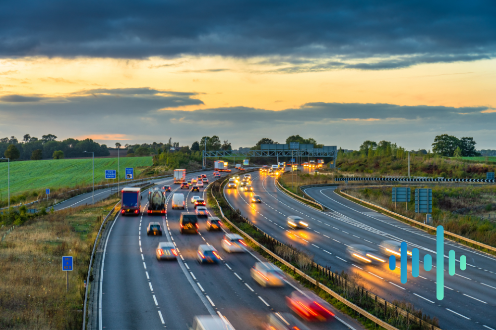 Busy motorway curving through countryside at sunset with streaking headlights, with a blue and teal waveform