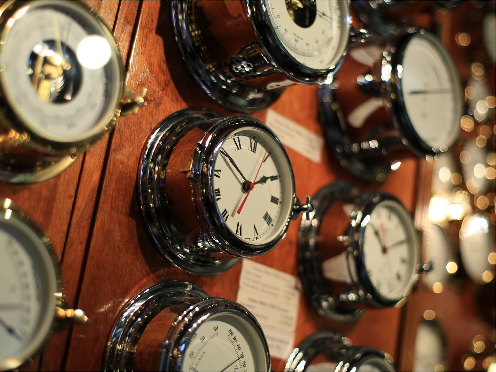 Rows of antique brass clocks and barometers mounted on a wooden wall