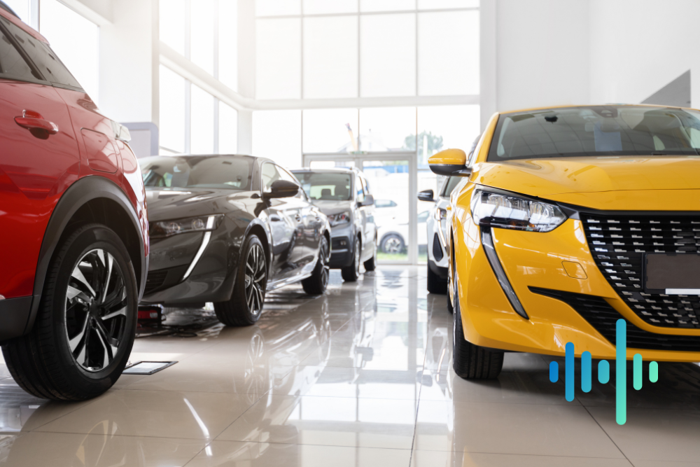 New cars, including red and yellow hatchbacks, parked in a bright car showroom, with a blue and teal waveform
