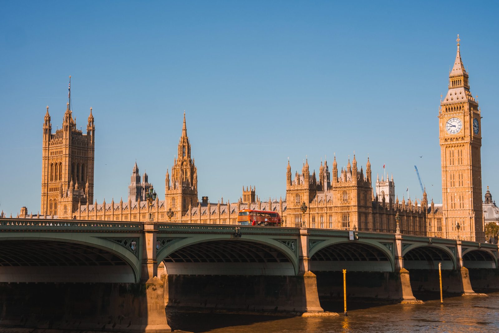 Houses of Parliament and Big Ben beside Westminster Bridge in warm sunlight under a clear blue sky