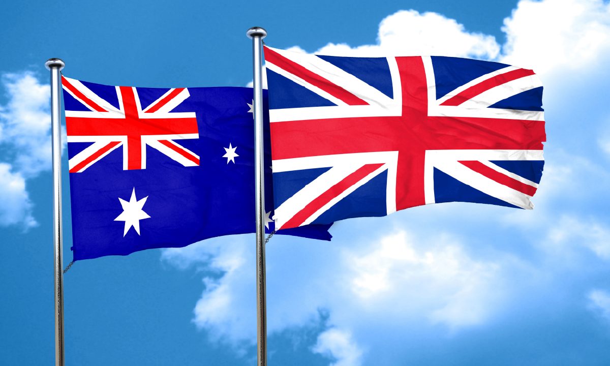 Australian and British flags flying side by side against a blue sky with white clouds
