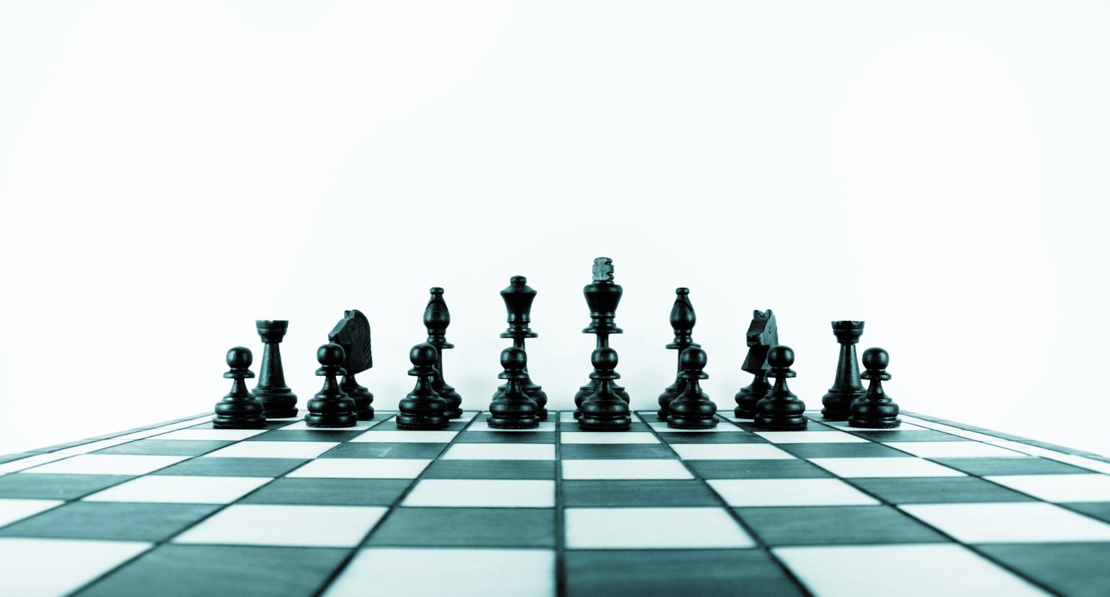 Row of black chess pieces lined up on a black and white chessboard against a white background