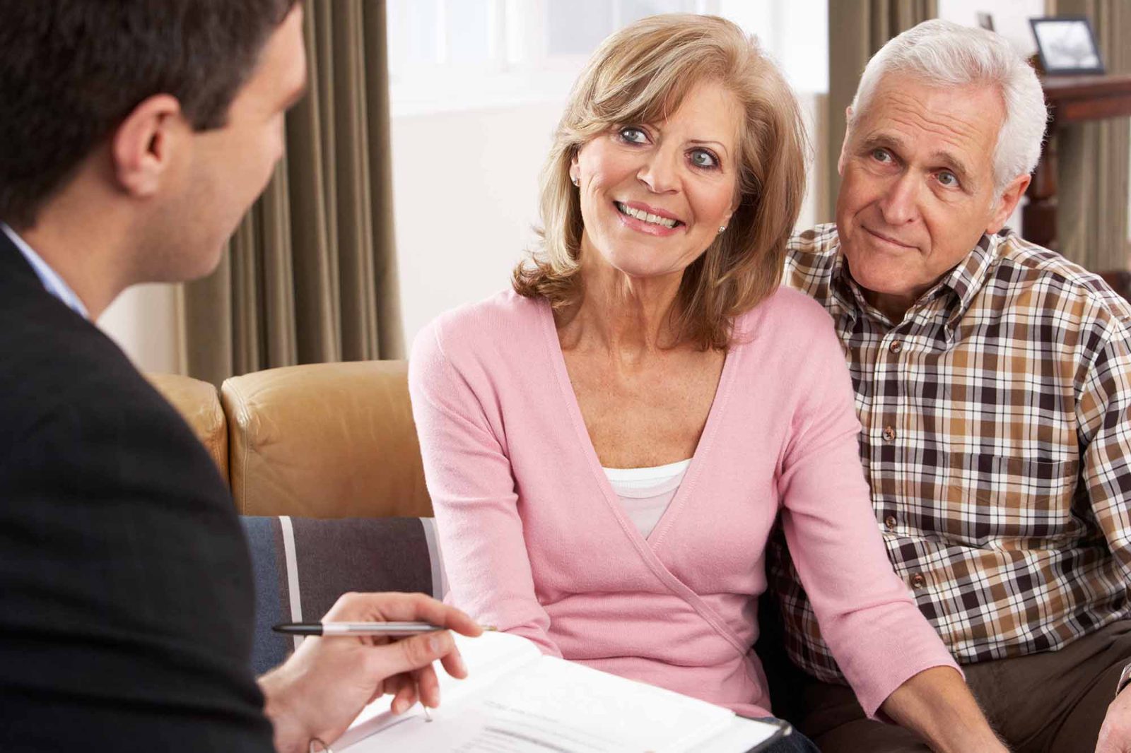 Financial adviser holding a pen and papers, meeting a smiling older couple on a sofa at home