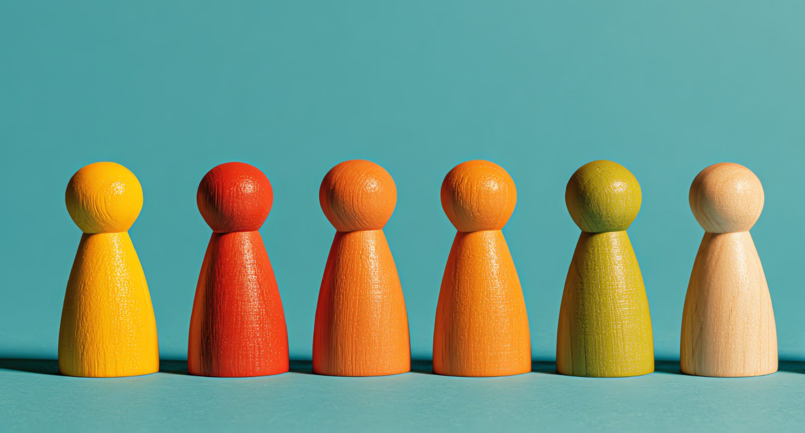 Row of six wooden peg figures in yellow, red, orange, green and natural wood against a teal wall