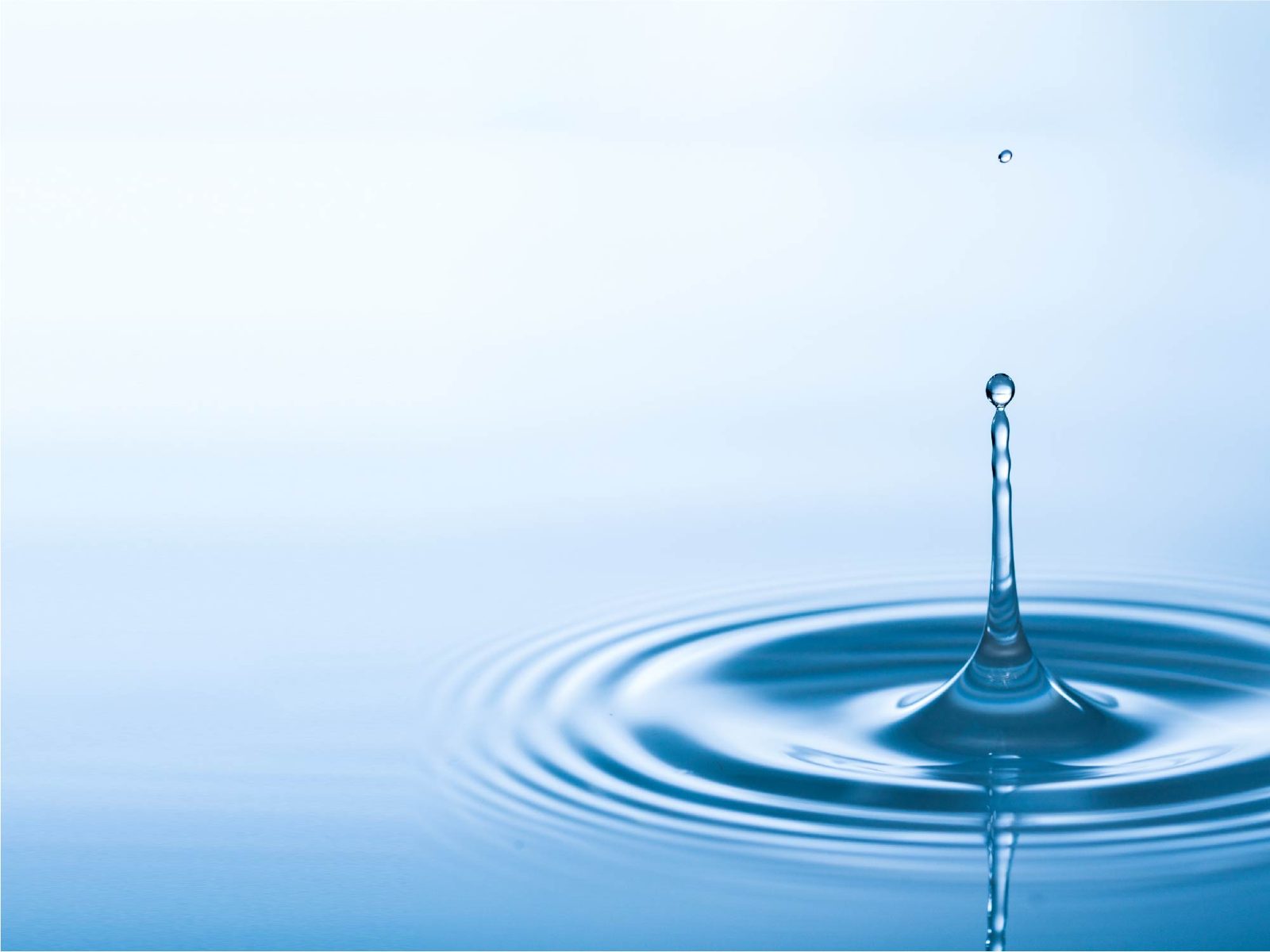 Water droplet falling into still blue water and sending out circular ripples