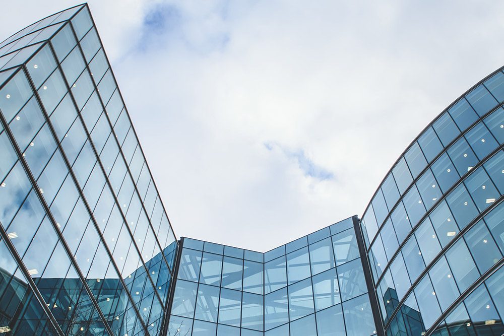 Low-angle view of curved glass office buildings reaching into a cloudy sky