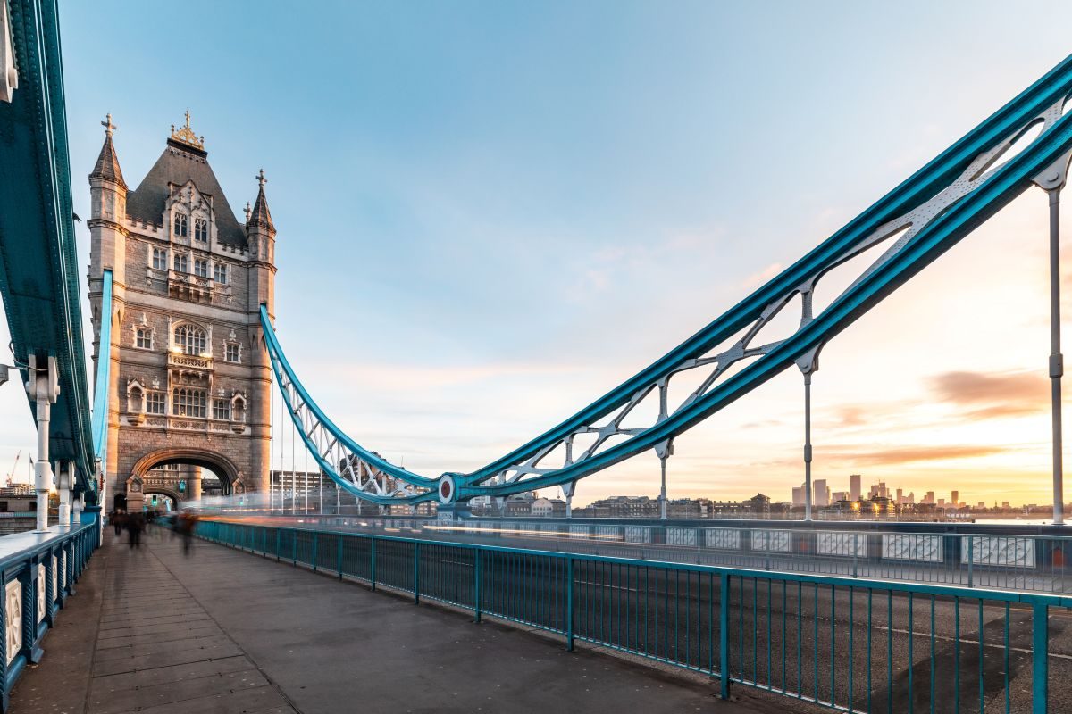 Walkway across Tower Bridge with its blue suspension chains and a Gothic tower at sunrise