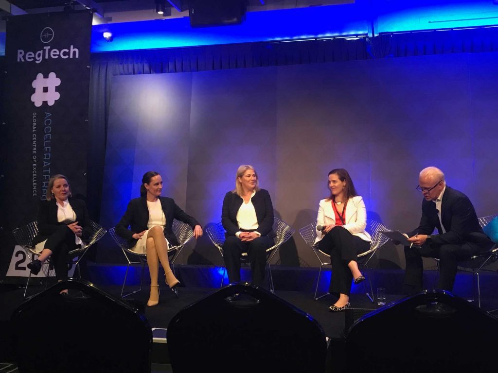 Five panellists, four women and one man, seated on a blue-lit stage beside a RegTech event banner