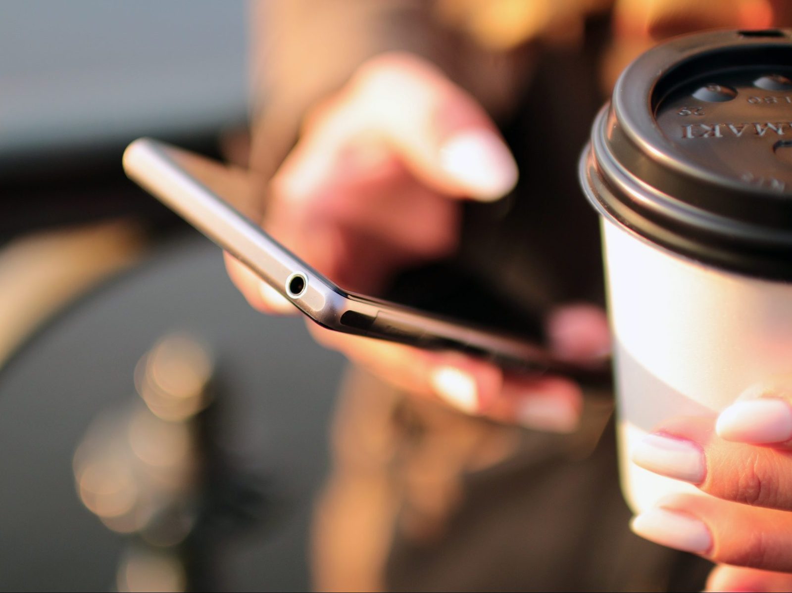 Close-up of hands holding a smartphone and a takeaway coffee cup