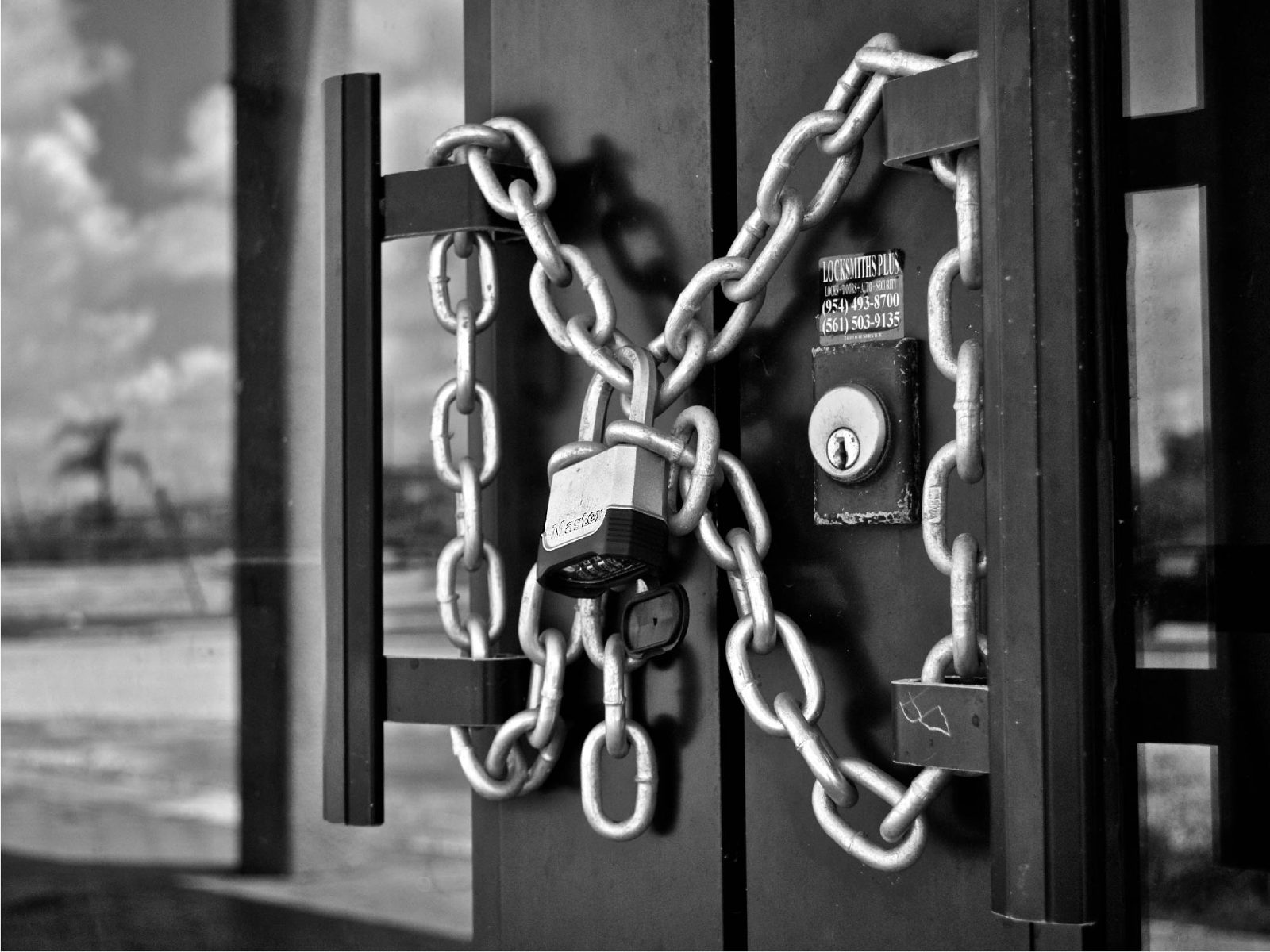 Black-and-white close-up of door handles wrapped in a heavy chain and padlock