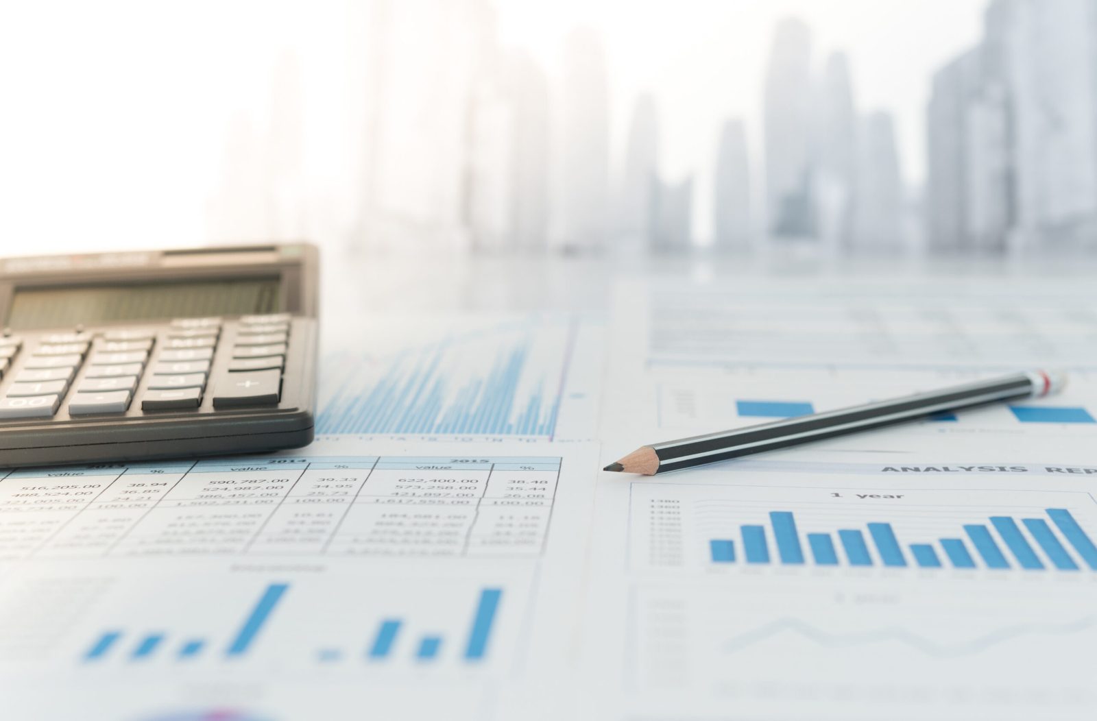 Calculator and pencil on printed financial charts in bright, hazy light with a faint city skyline
