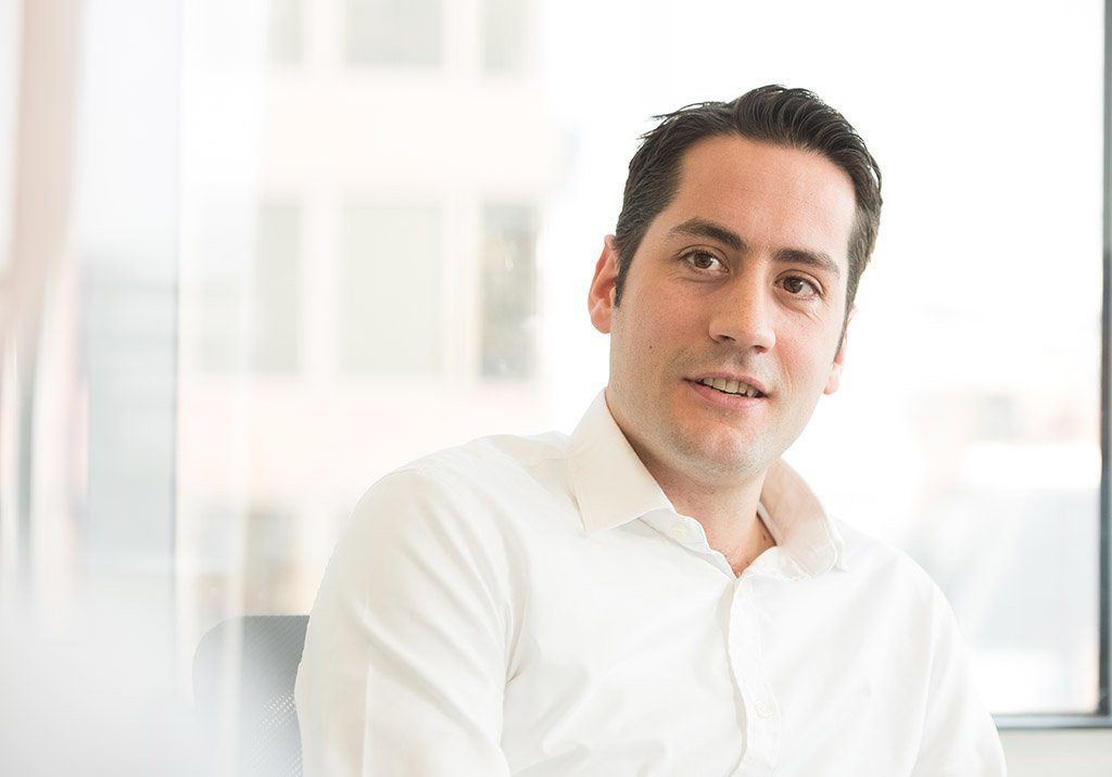 Jonathan Drechsler, a man with short dark hair in an open-necked white shirt, in a bright office