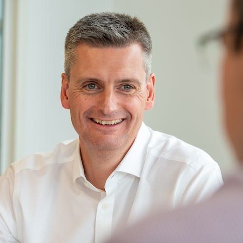 Joe Norburn smiling in an open-necked white shirt in a bright office