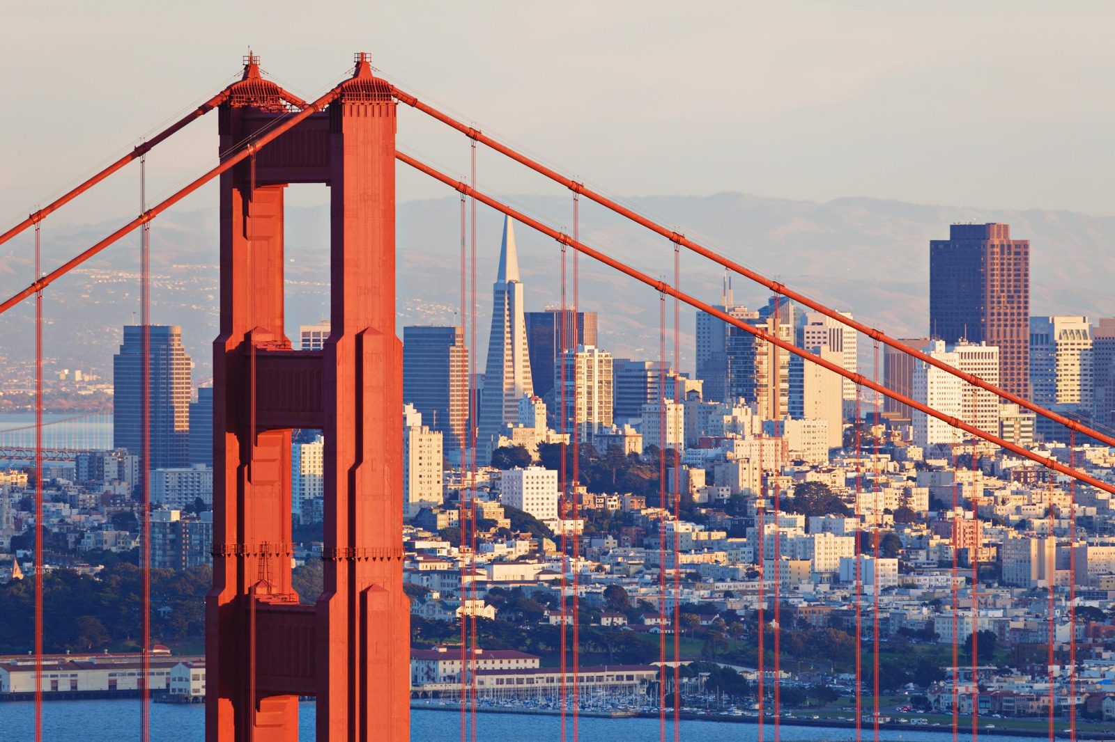 Red tower and cables of the Golden Gate Bridge with the San Francisco skyline behind