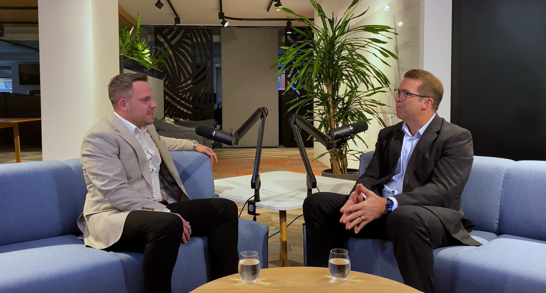 Garry Evans and Thomas Richter talking on blue sofas with podcast microphones in a modern office lounge