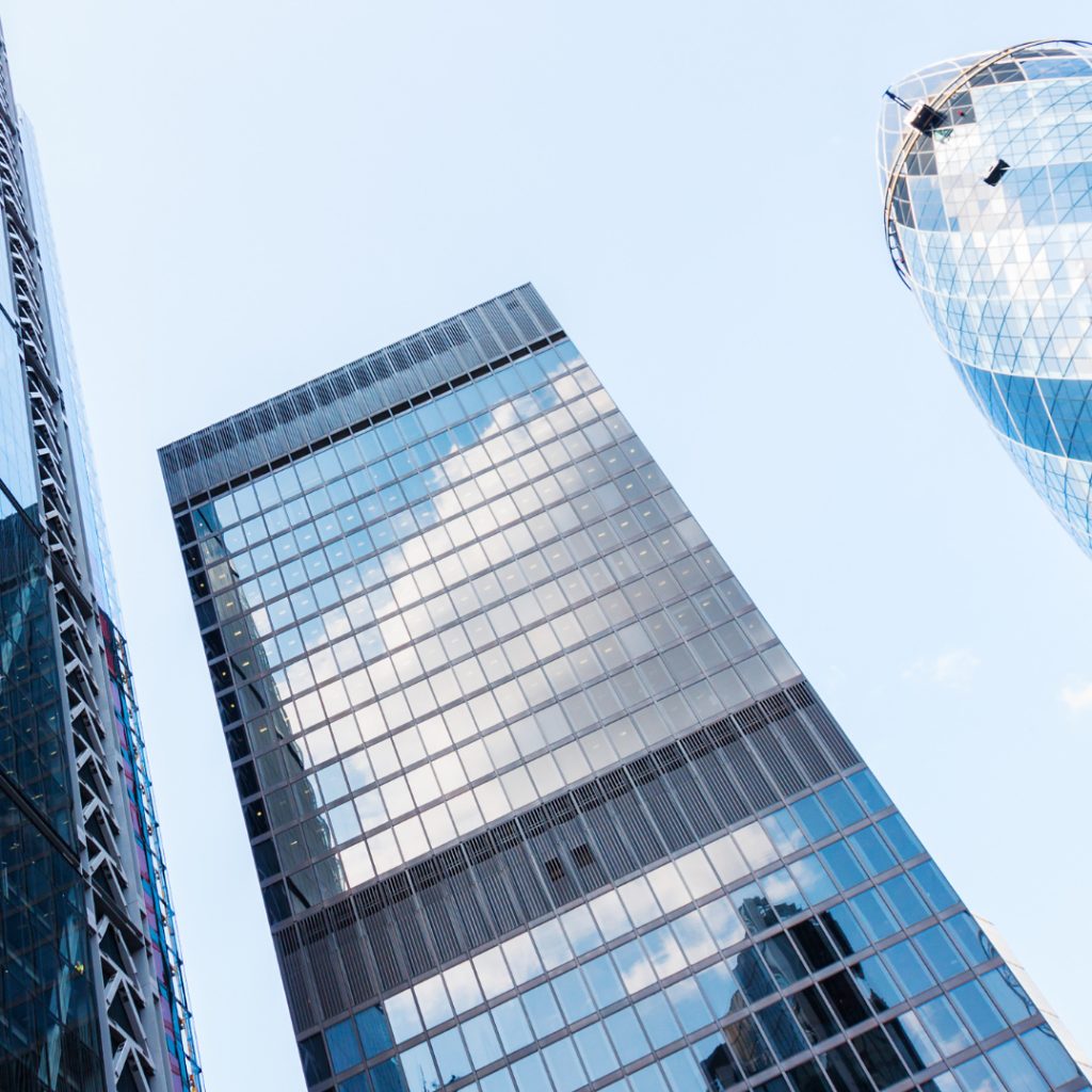 Low-angle view of glass office towers and the edge of the Gherkin against a pale blue sky