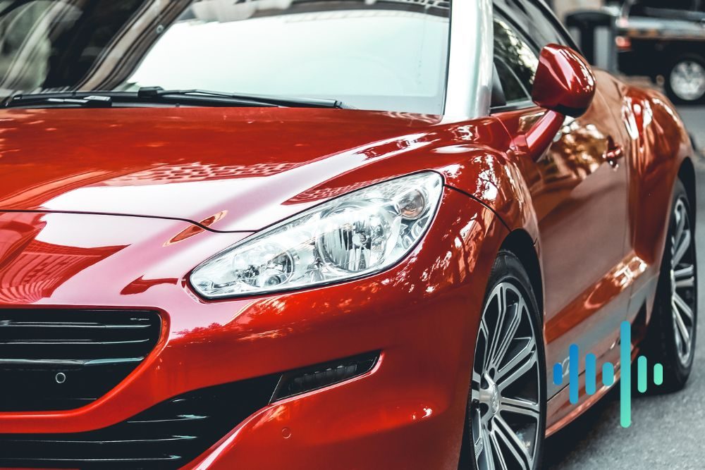 Close-up of the front and headlight of a glossy red car in a showroom, with a blue and teal waveform