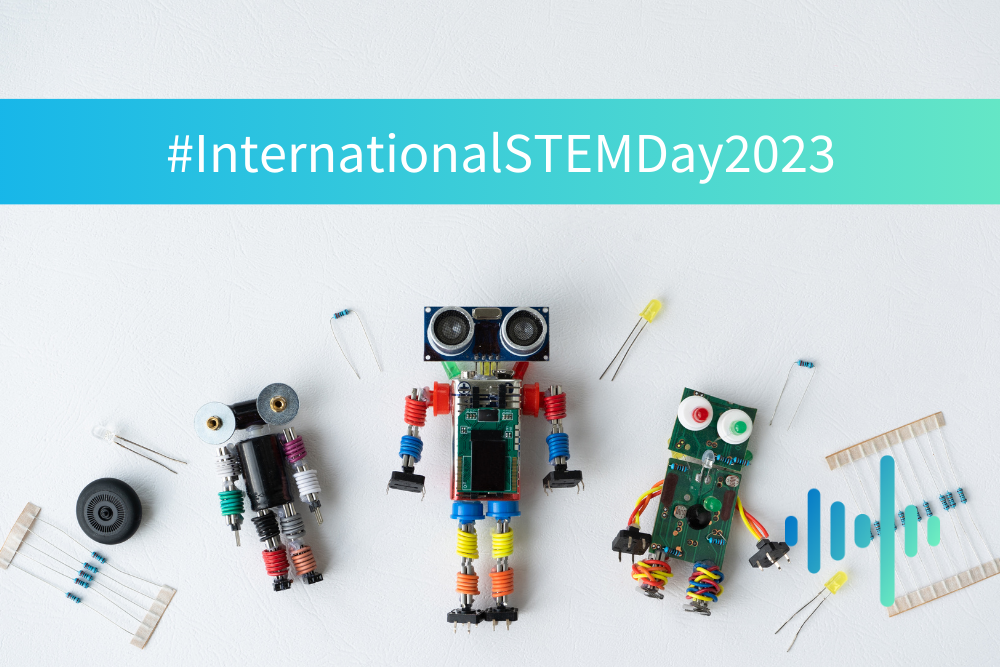 Small robots built from electronic components and wires on a white surface beneath an International STEM Day banner