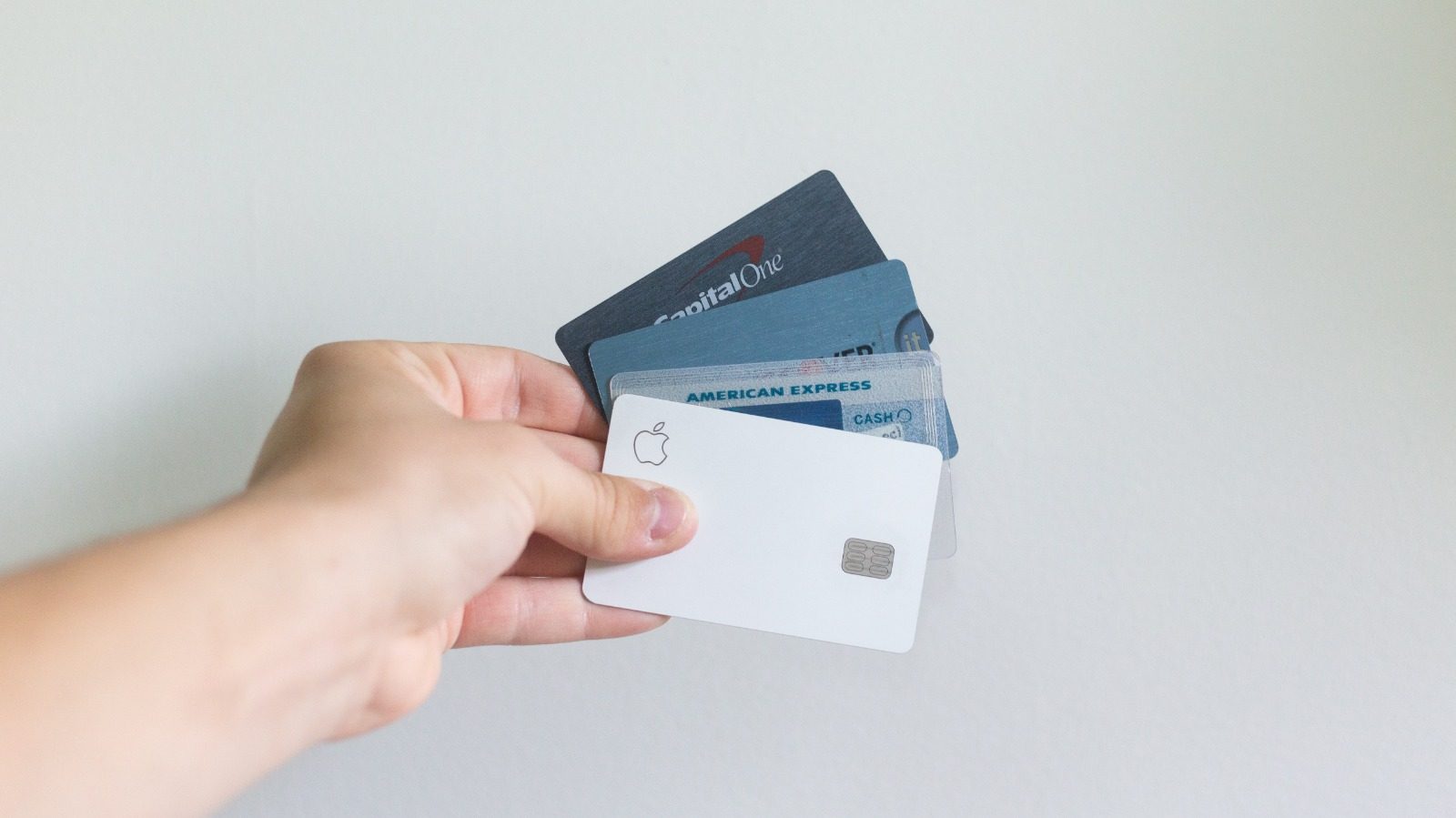 Hand holding a fan of payment cards against a pale wall, with a plain white card at the front