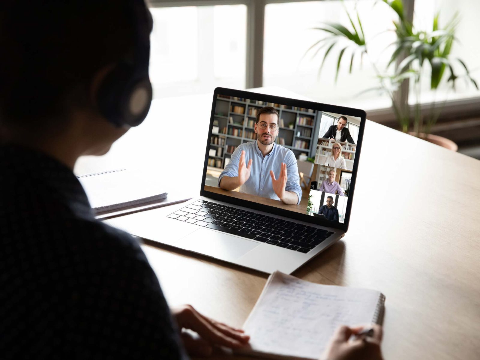 Person taking notes during a video call on a laptop showing a grid of meeting participants