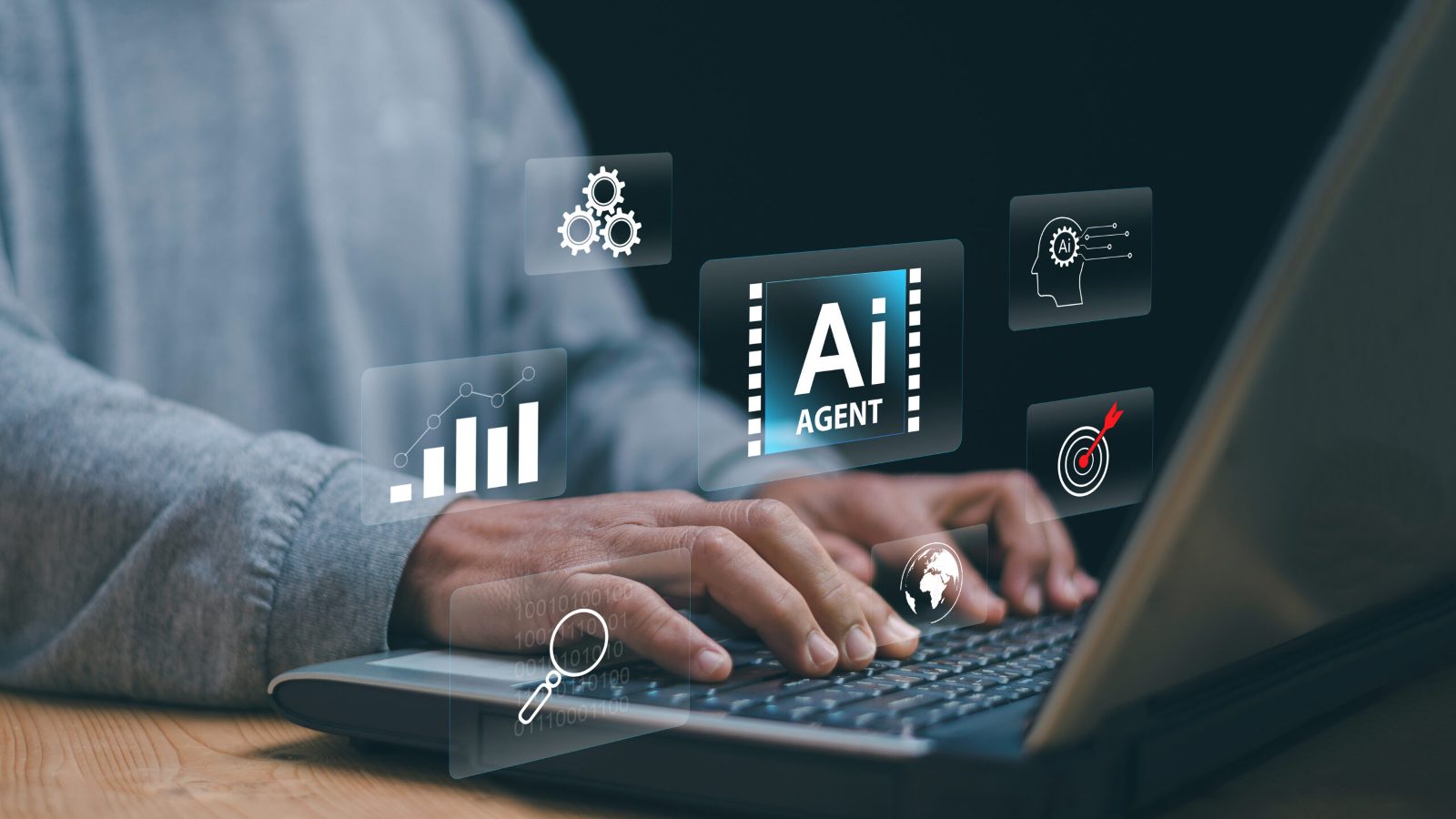 Hands typing on a laptop beneath floating icons of an AI agent, gears, a chart and a target